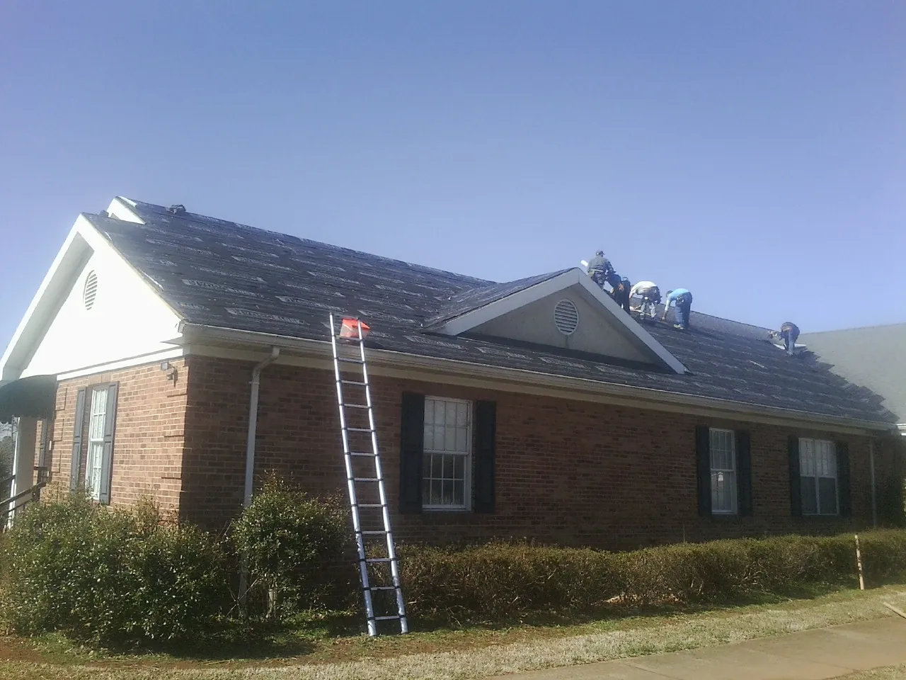 Crew tearing shingles off a brick ranch roof with a ladder set — Emergency Roof Repair work by our crew in Union City