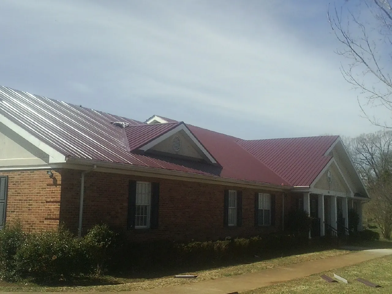 Red metal roof with gabled entries on a long brick building, from a Hail Damage Roof Repair job in Union City