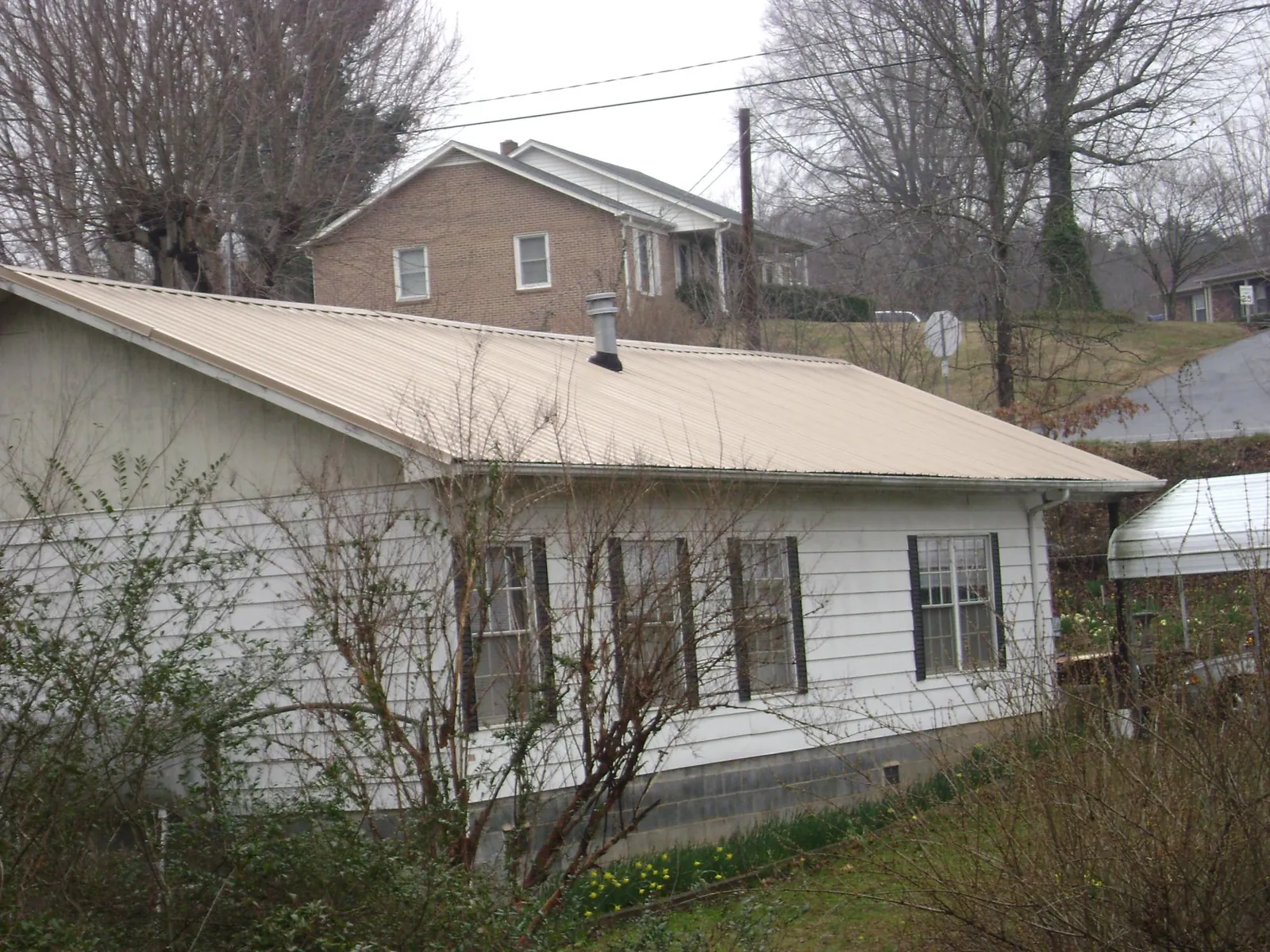 Tan metal roof on a white sided house set into a hillside — Commercial Roofing by Roofing Brothers in Union City